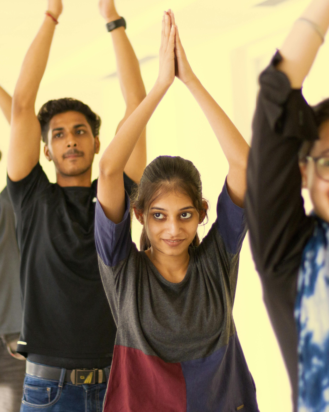 Group of young people practicing yoga with hands raised together, focusing on balance and coordination in a class setting.