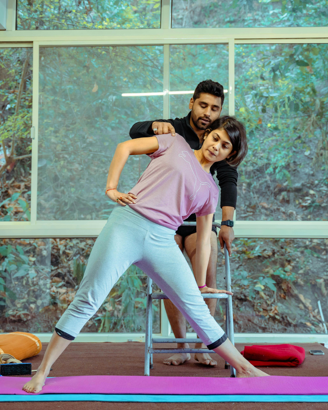 Yoga instructor helping a woman perform a side stretch posture indoors, ensuring proper alignment and technique.