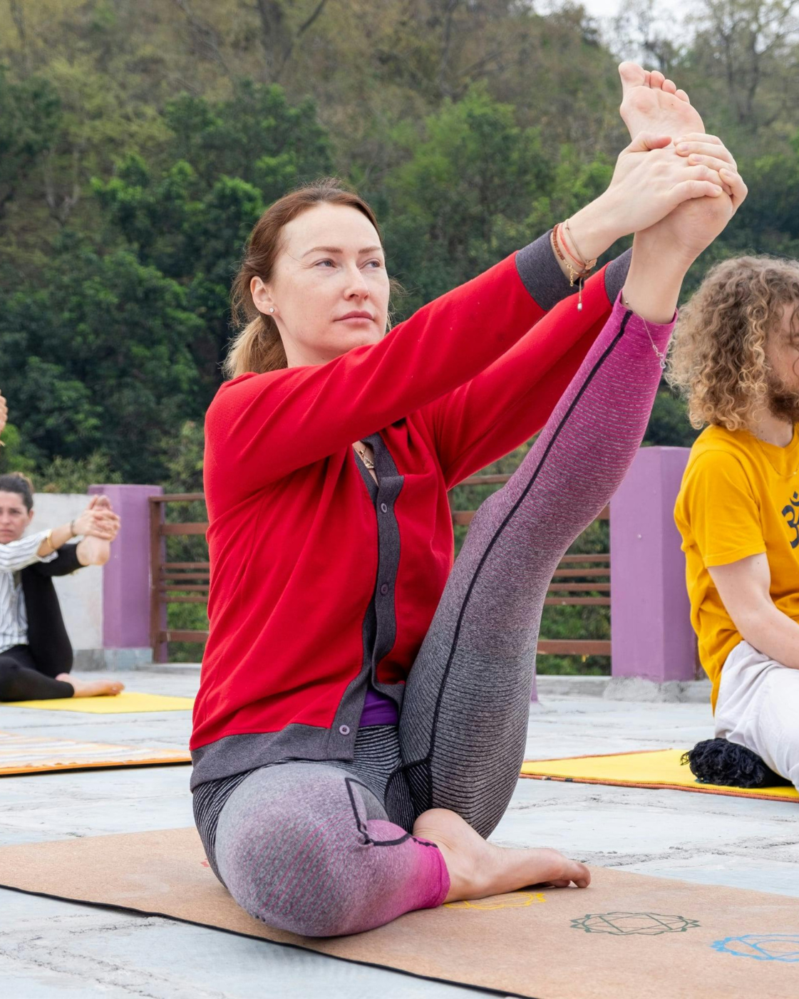 Yoga trainer assisting a woman in a deep backbend stretch on a mat outdoors, improving flexibility and posture.