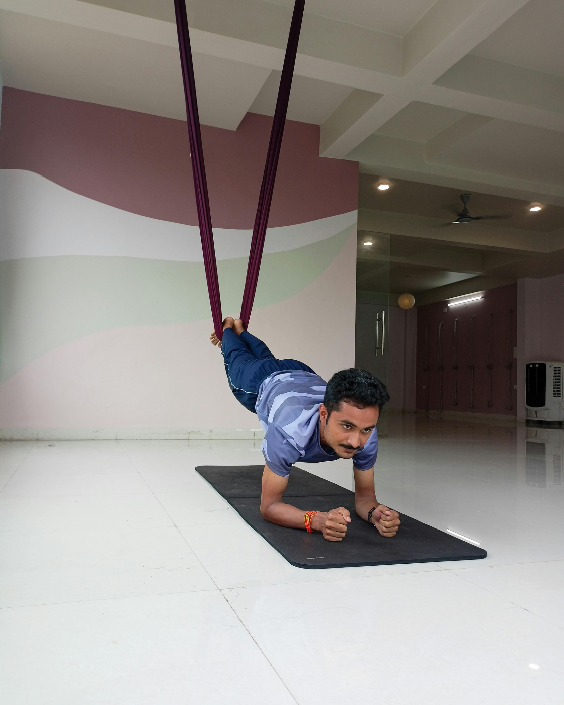 Man performing a suspended plank exercise using aerial yoga straps, building core strength and balance indoors.