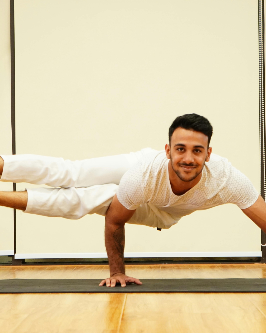 Man performing a challenging arm balance yoga pose indoors, demonstrating strength, control, and flexibility.