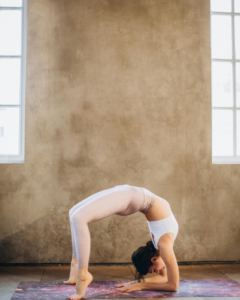 Woman performing an advanced backbend yoga pose on a mat, showcasing flexibility and core strength in a calm indoor space.